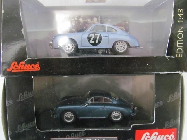 Two model Porsche 356 cars in boxes: a light blue race car with number 27, and a dark blue one.