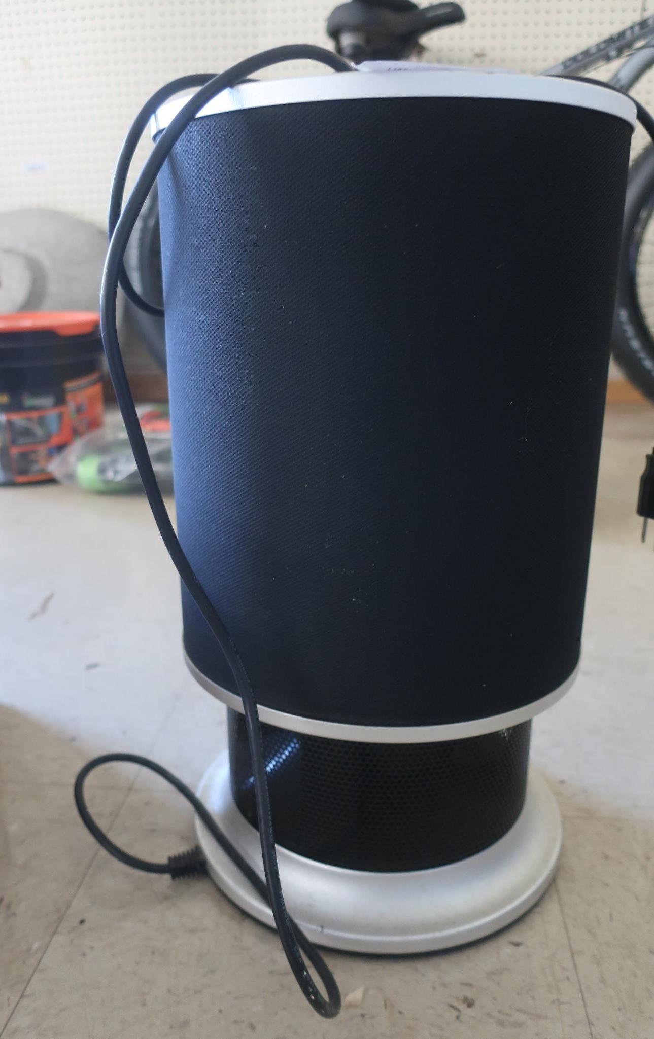 Cylindrical black speaker with silver trim and base. Black cord extends from the speaker.