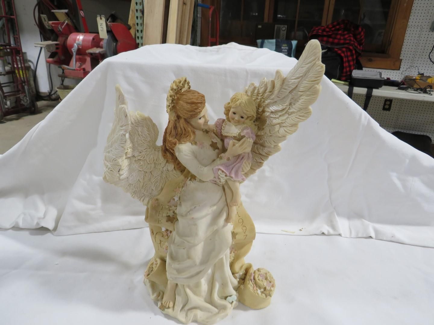 Statue of angel figure with outstretched wings, holding a small child. Beige and off-white colors.