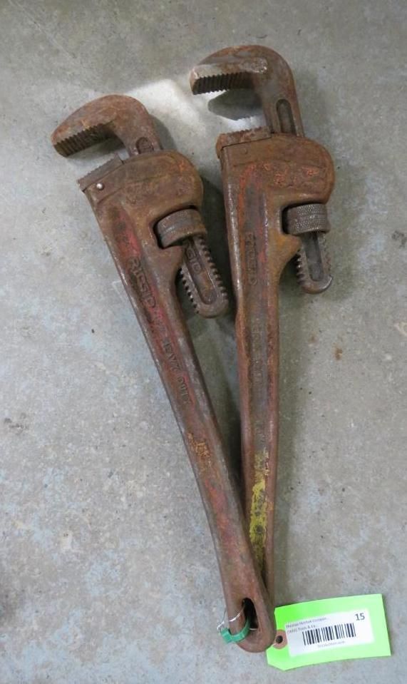 Two pipe wrenches on a concrete surface, with a green tag.