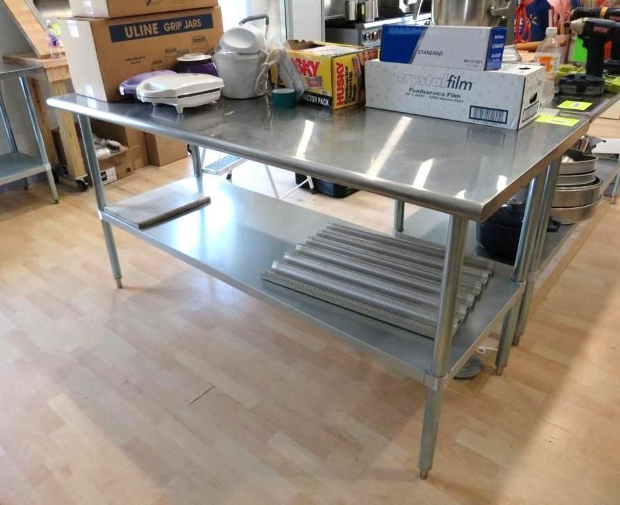 Stainless steel work table with a lower shelf, holding various kitchen supplies.