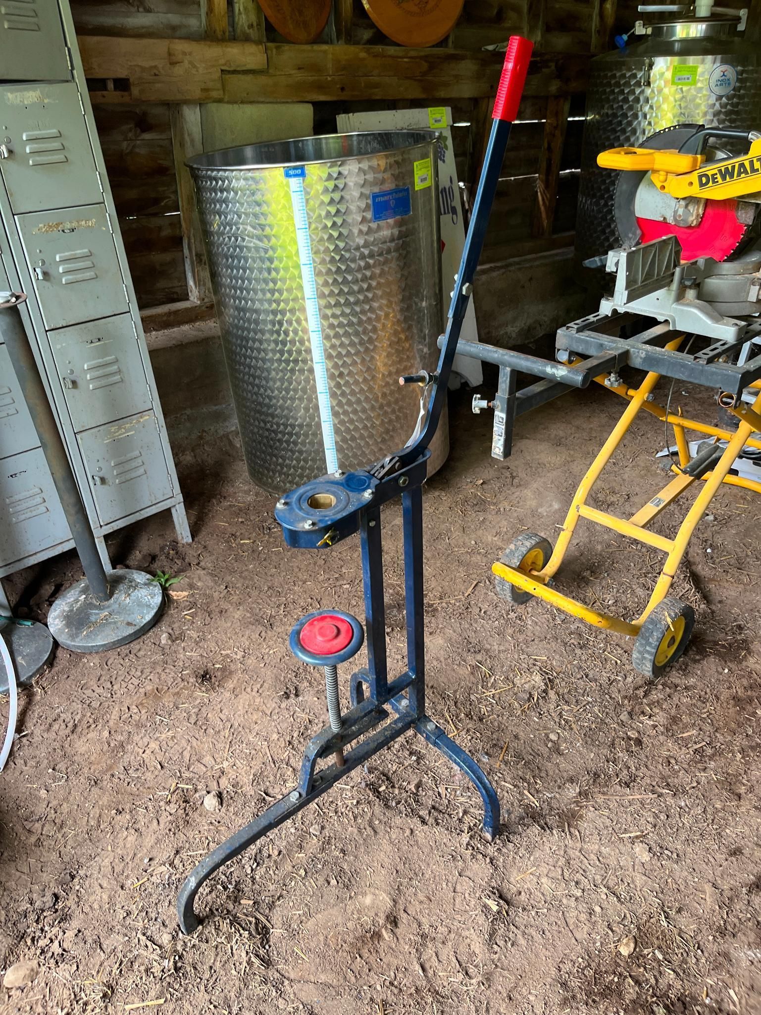 Bottle capper with red handle and blue base, indoors near stainless steel tanks and a saw.