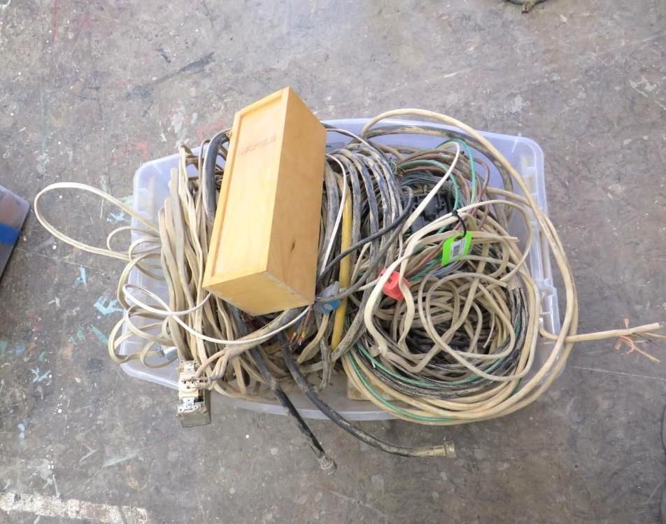 Electrical cords and a wooden box inside a clear plastic bin on a concrete surface.