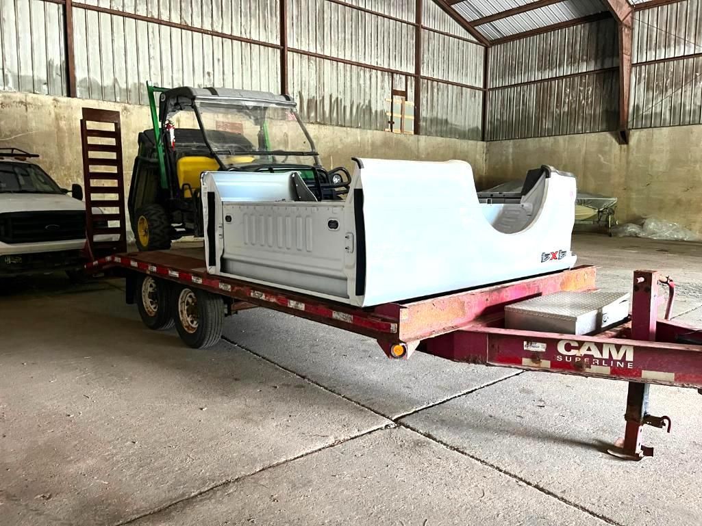 Trailer with a white truck bed and a green utility vehicle inside a barn.