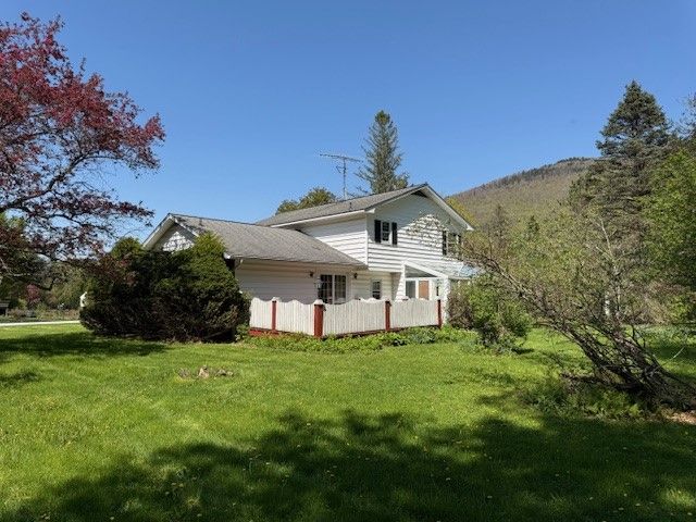 White two-story house with a small porch, set on a green grassy lawn under a clear blue sky.