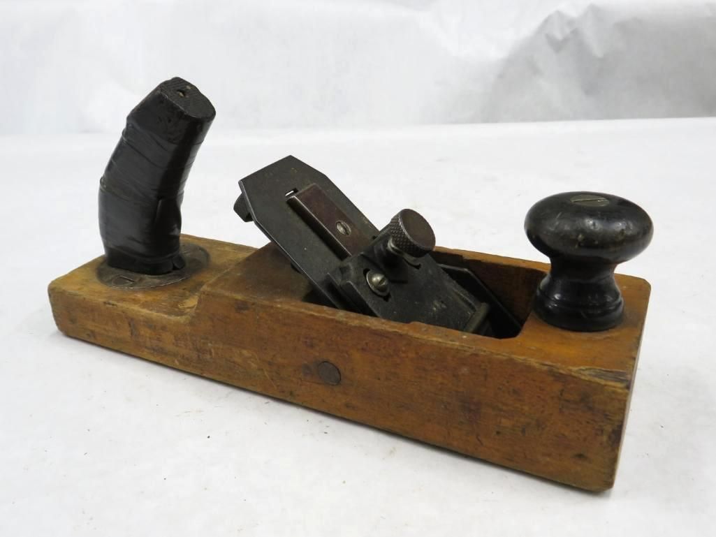 Wooden hand plane with a dark handle and knob, set on a white surface.