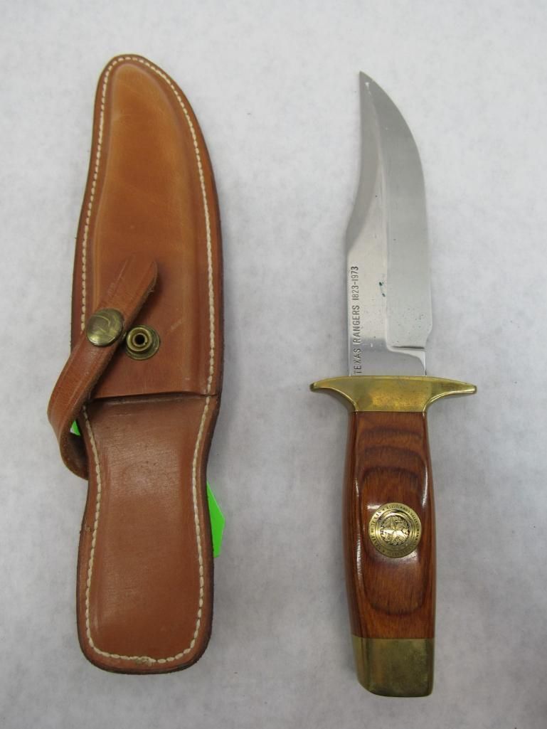 Brown leather sheath and hunting knife with wooden handle and brass accents on white background.