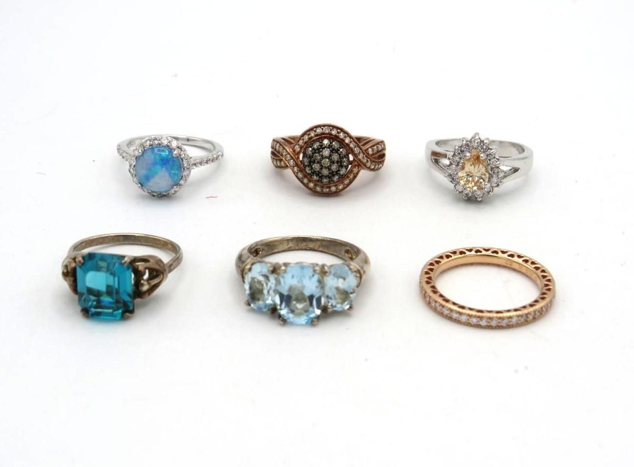 Six various gemstone rings on a white surface; blue, yellow, and clear stones.