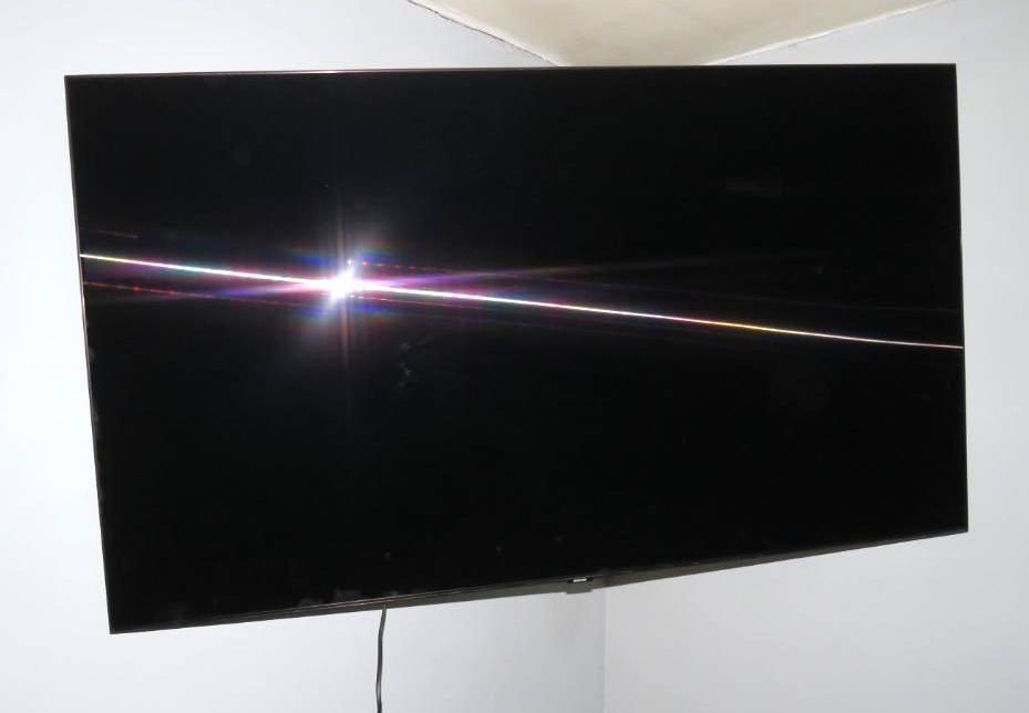 Black flat-screen TV mounted on a white wall in a corner; light reflecting across the screen.