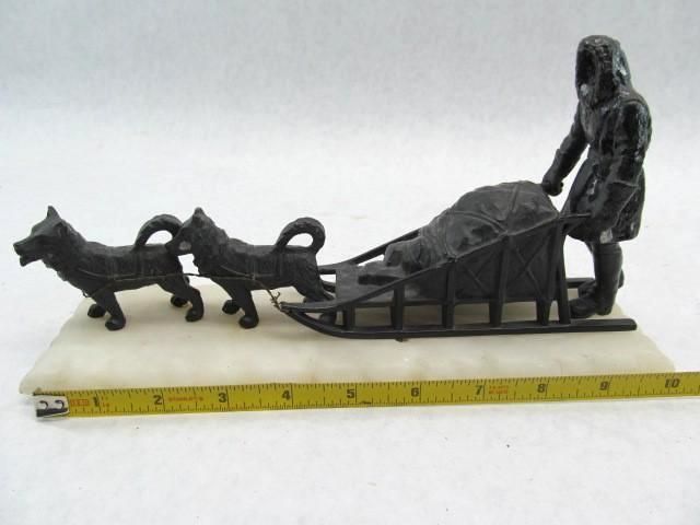 Dog sled with driver, two dogs pulling, load in the sled, snow-covered ground.