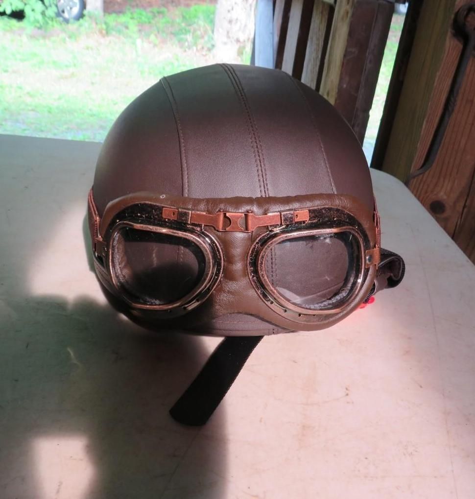 Brown leather motorcycle helmet with goggles, sitting on a table.