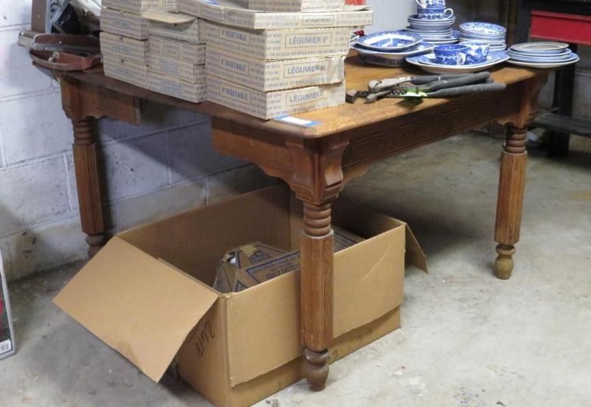 Wooden table with boxes of items, several dishes and tools, in a basement setting.