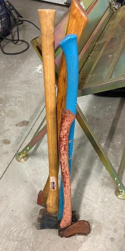 A group of axe handles, three wooden and one blue, stand upright against a metal frame.
