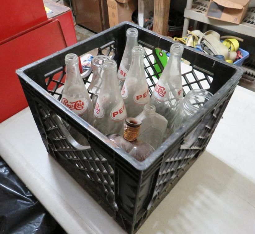 Black crate filled with empty Pepsi and other glass bottles.