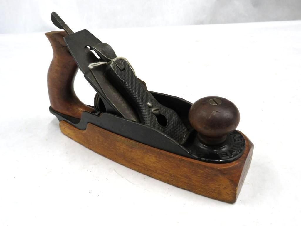 Wooden hand plane with a dark-colored iron blade and handle, on a white surface.