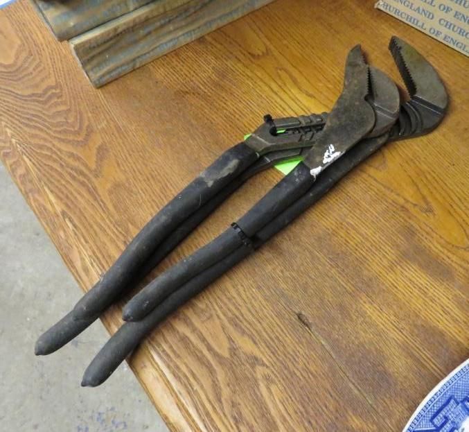 Pair of large adjustable pipe wrenches on a wooden table.