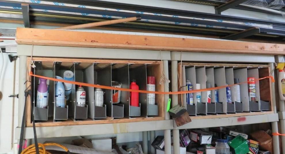 Spray paint can organizers mounted on a shelf, with cans of various colors stored inside.