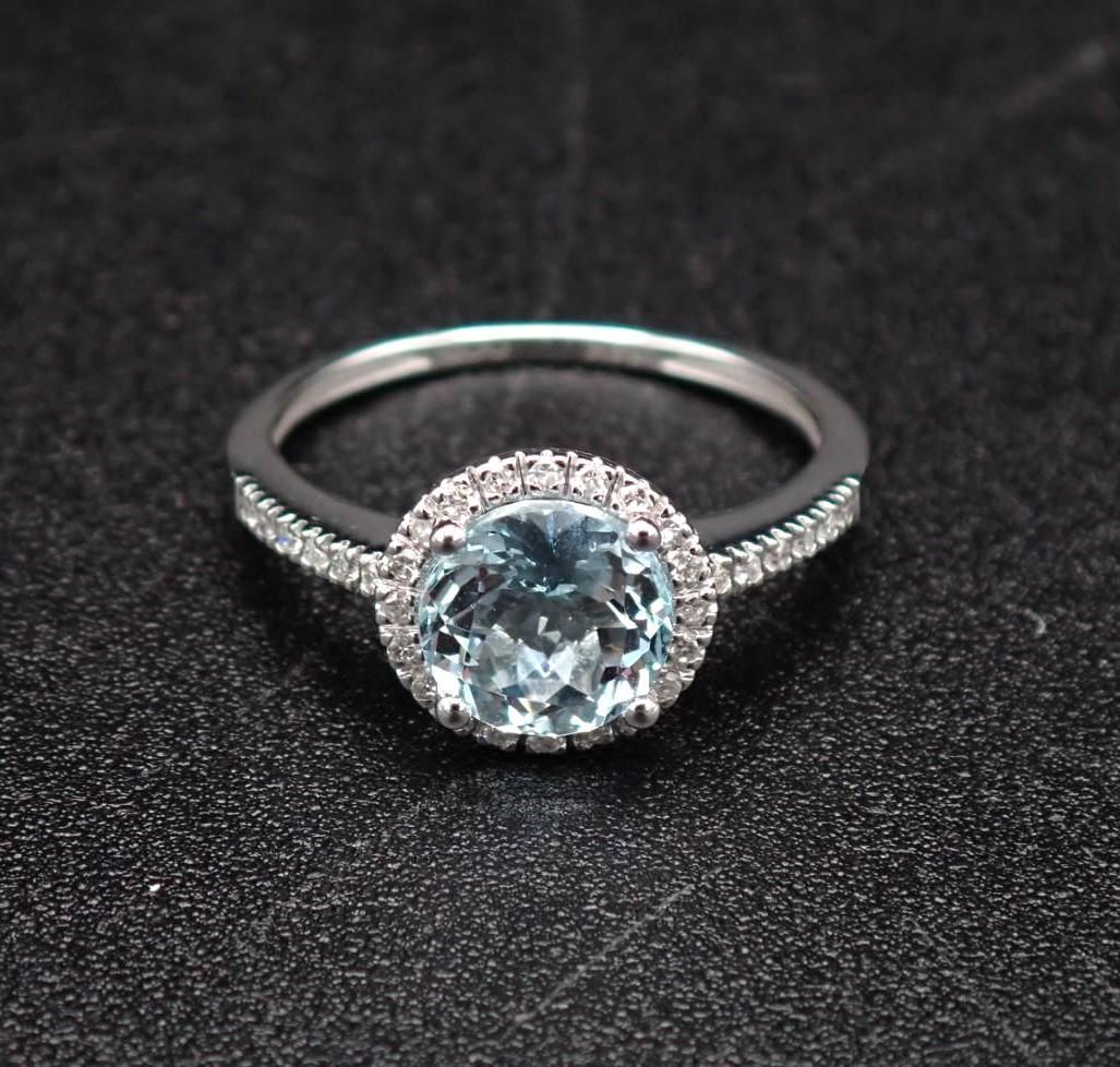 Silver ring with a round, light blue gemstone center, surrounded by smaller white stones.