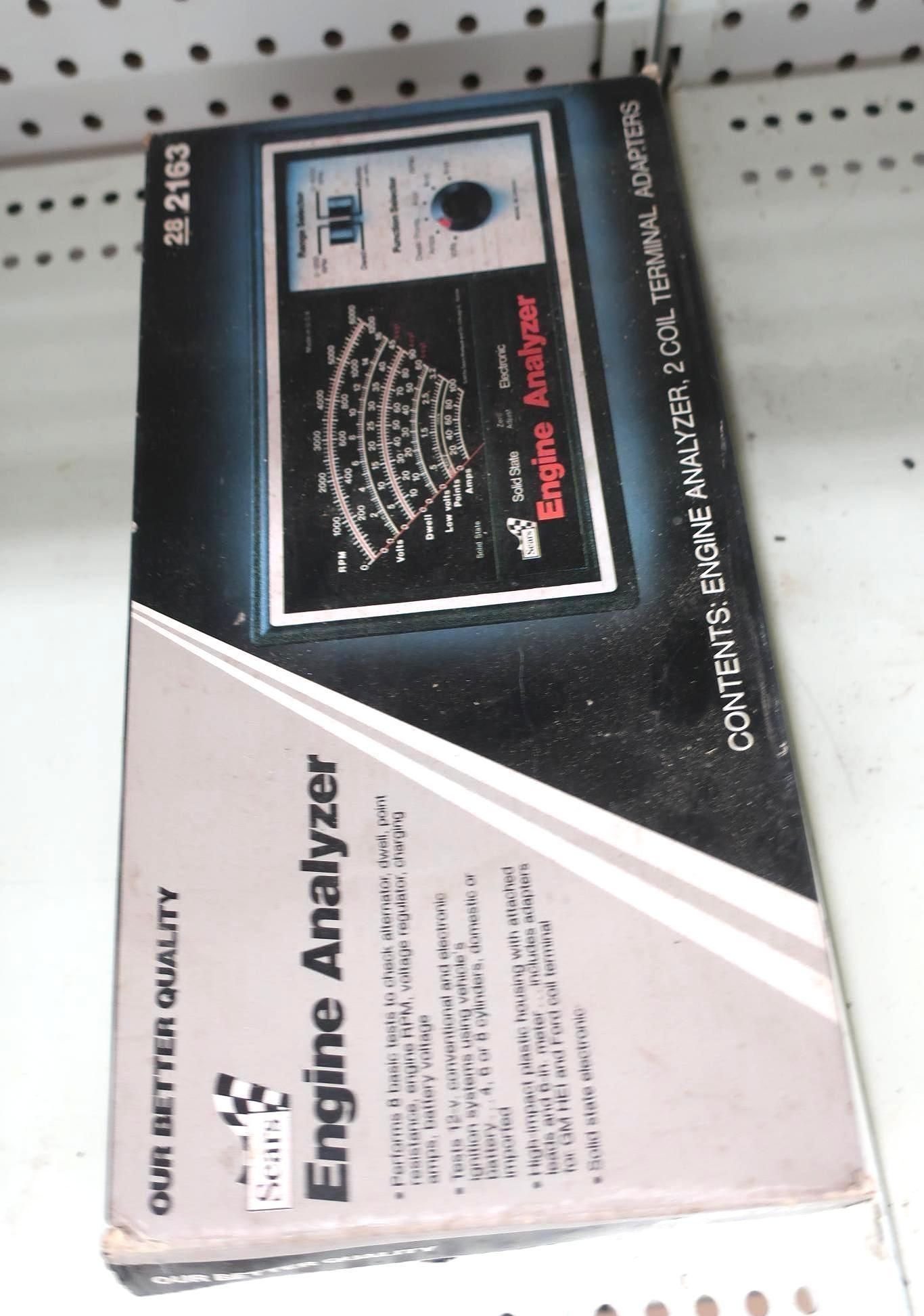 Box for an engine analyzer tool with a gauge and dial. Black, white, and gray colors.