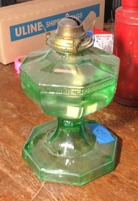Green glass antique oil lamp on a wooden surface, with a brass top and hexagonal base.