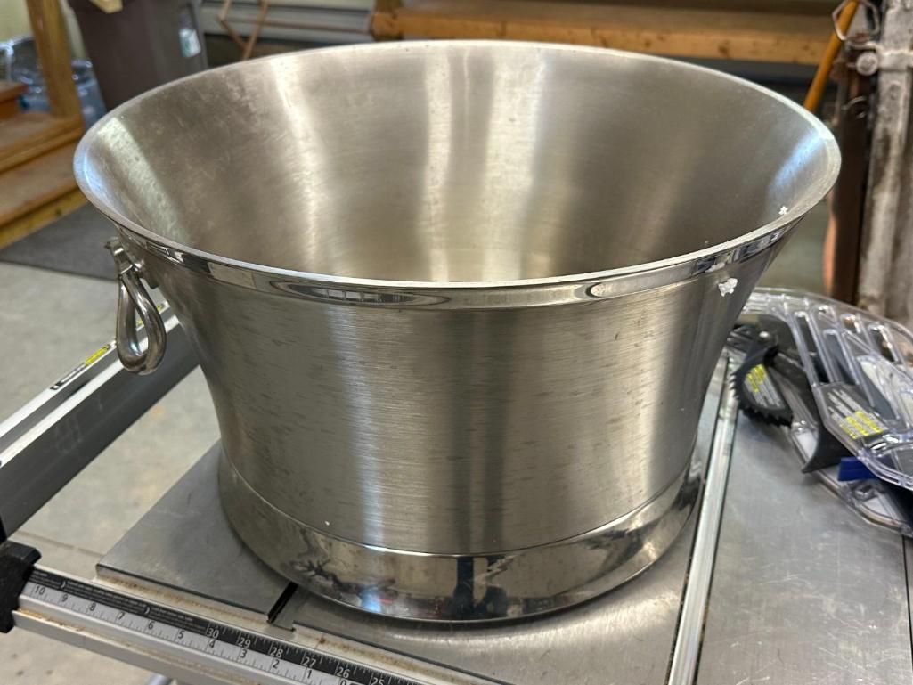 Large, silver metal ice bucket with handles, sitting on a table.