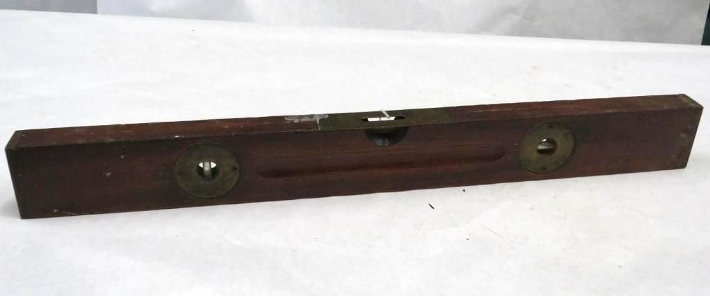 A wooden level tool with brass circles and a bubble window, set on a white surface.