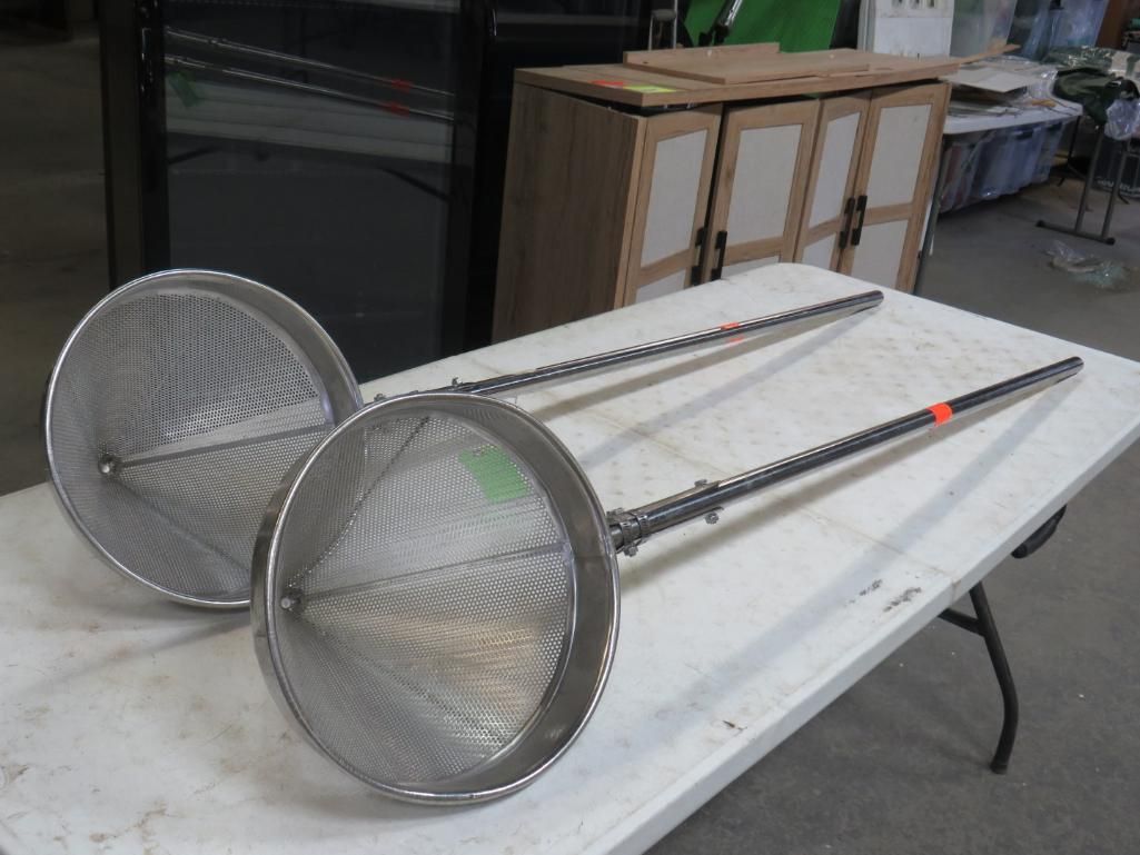 Two stainless steel conical strainers with long handles, resting on a white table.