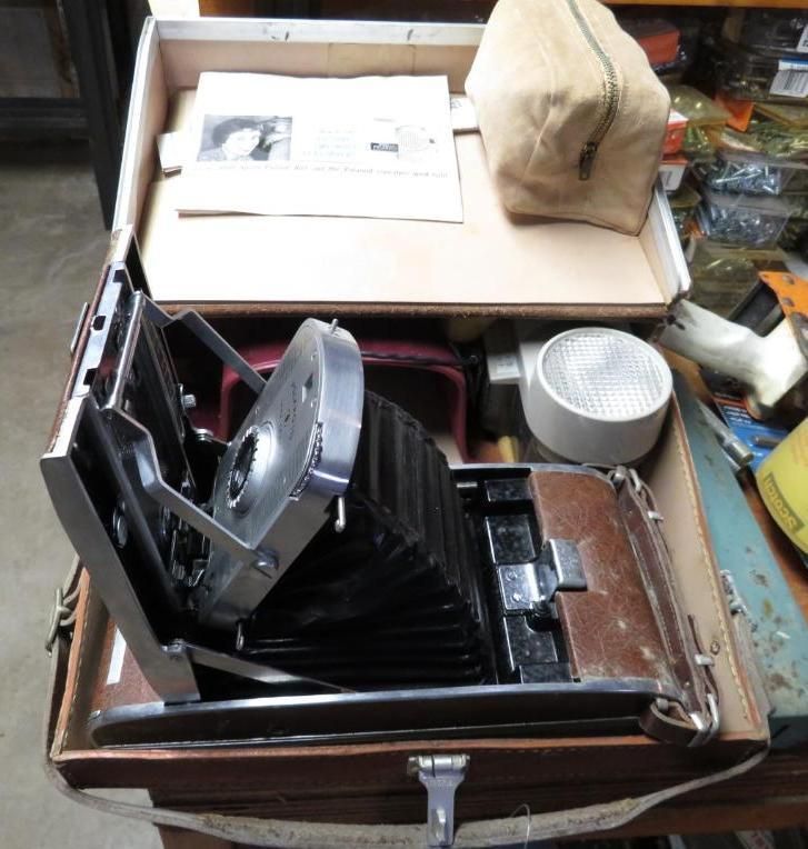 Vintage Polaroid camera in open case, with flash, manual, and bag.