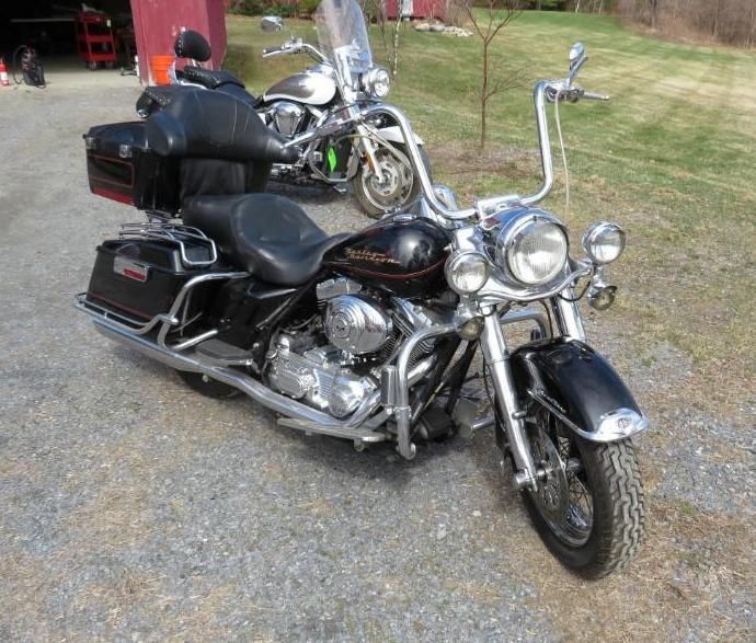 Black Harley-Davidson motorcycle with tall handlebars parked on gravel.