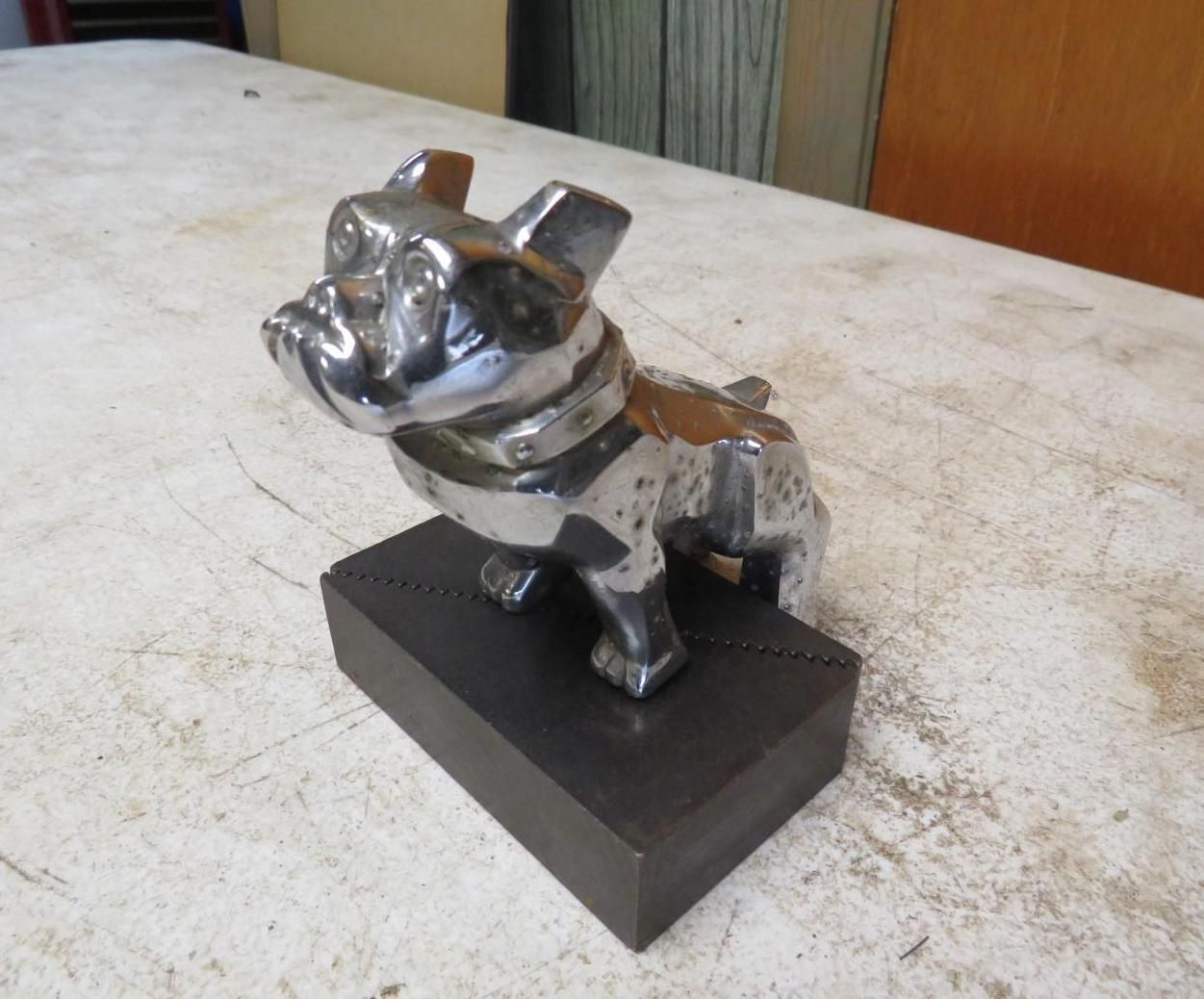 Chrome bulldog hood ornament on a dark rectangular base, sitting on a white surface.