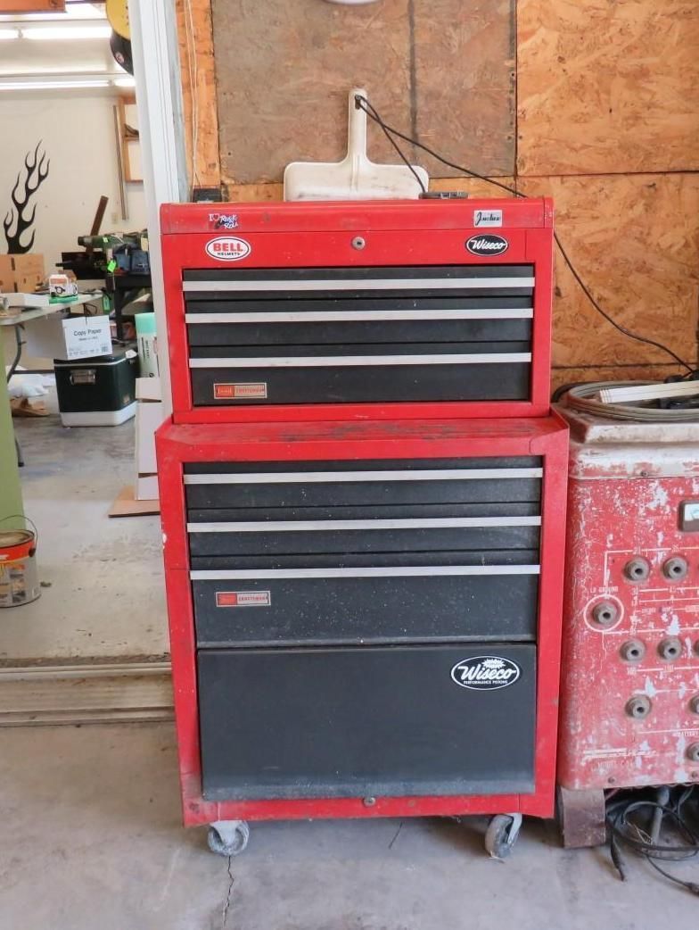 Red and black tool chest with multiple drawers, sitting on wheels.