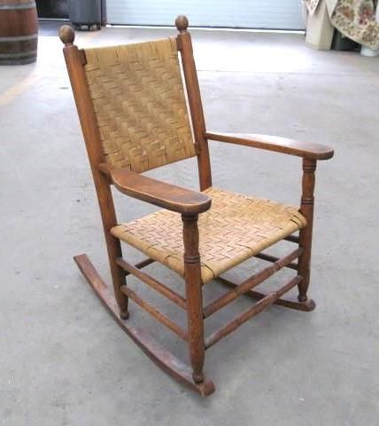 Wooden rocking chair with woven seat and back on a concrete floor.
