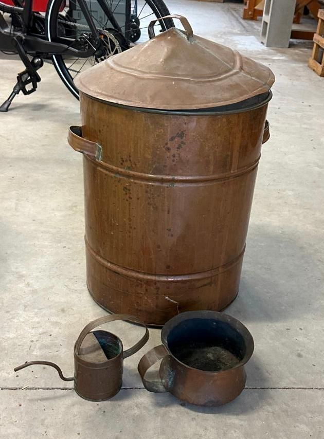 Copper trash can with lid, watering can, and bucket on concrete floor.