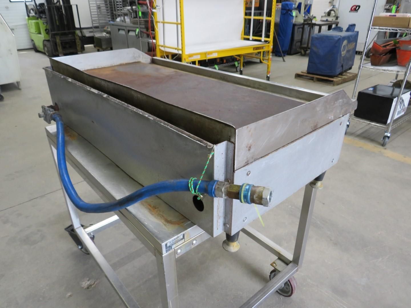 Stainless steel commercial griddle on a wheeled cart, connected to a blue hose.