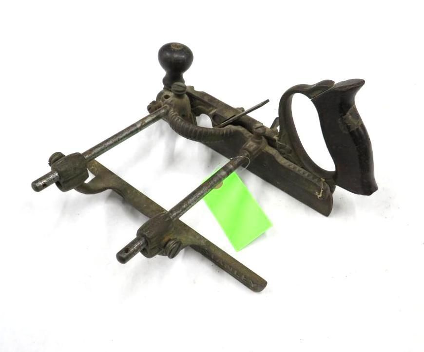 Antique woodworking tool, plane, with a dark wooden handle, lever, and metal frame, set against a white background.