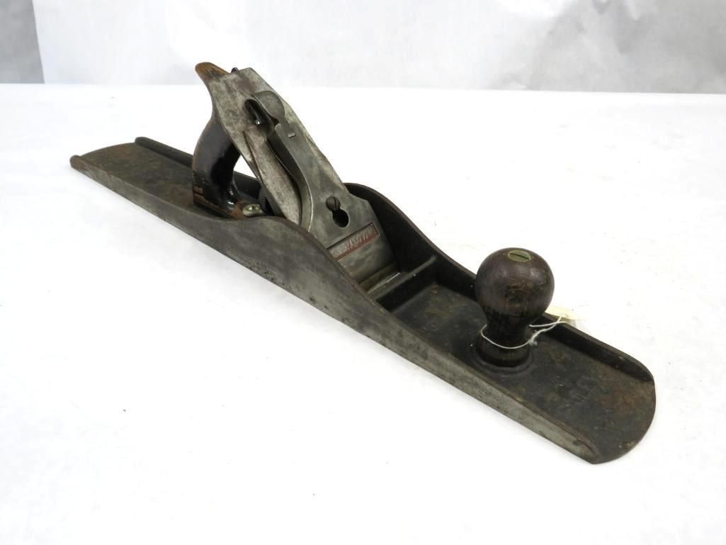 Hand plane, gray metal body with wooden handle and knob, set on a white surface.