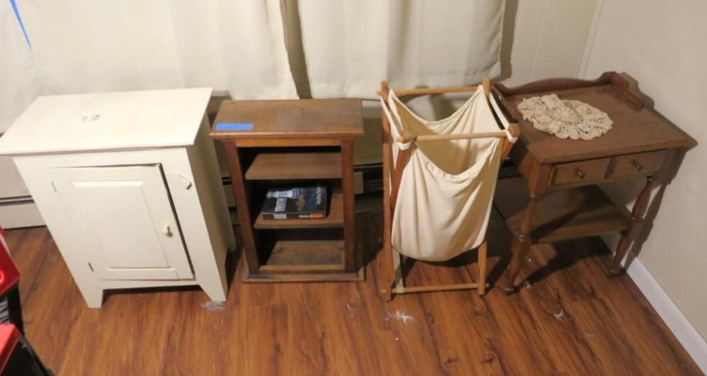 Four pieces of wooden furniture on a wood floor: a white cabinet, a shelf, a laundry hamper, and a small table.