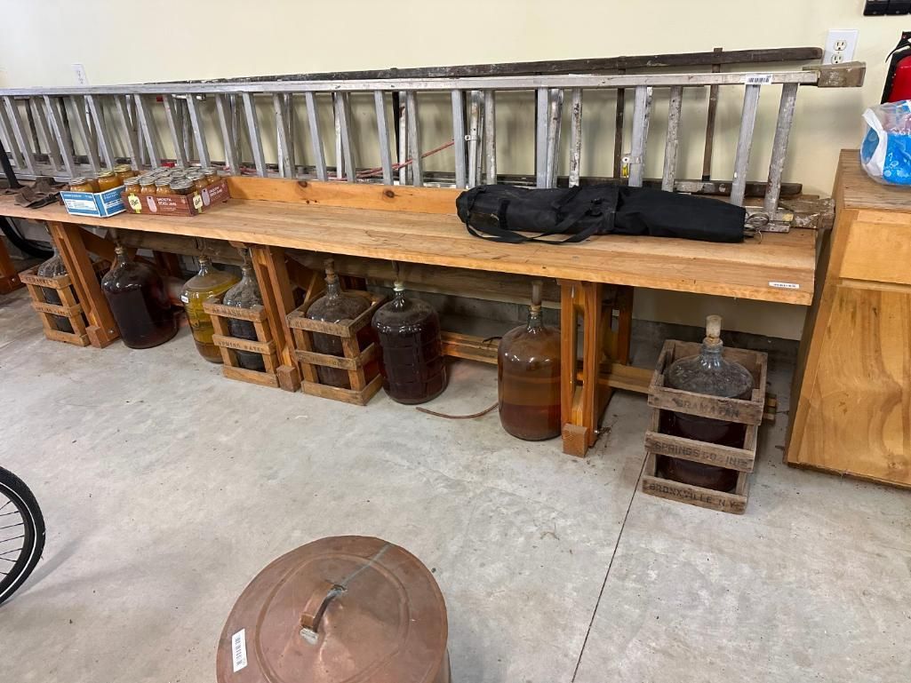 Wooden bench with glass jugs, ladder, and other items in a storage area.