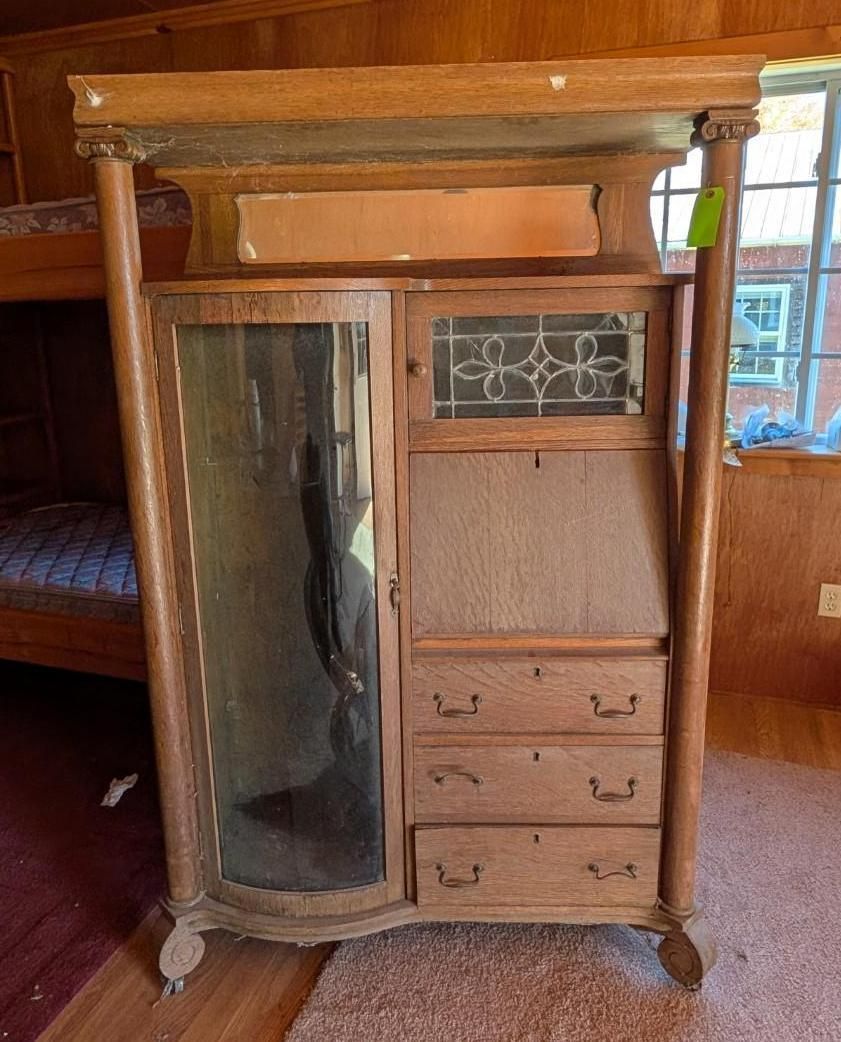 Antique wooden wardrobe with mirrored door and drawers in a wood-paneled room.