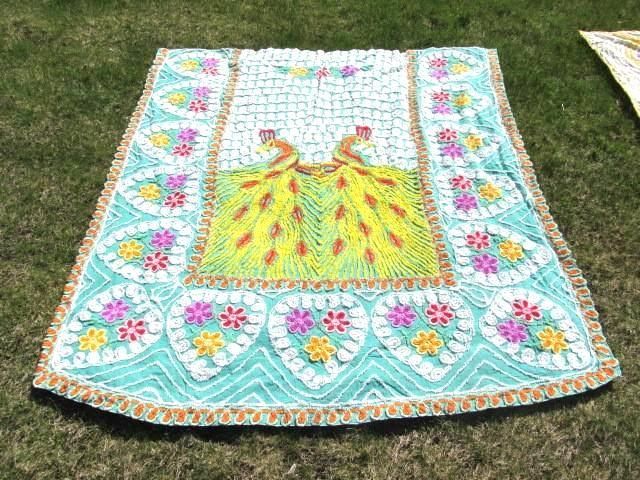 Embroidered fabric with peacock design, turquoise border, floral accents, and gold trim on grass.
