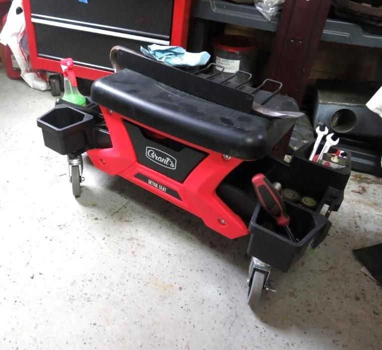 Red and black rolling mechanics seat with built-in storage and cup holders, in a garage.