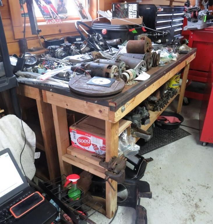 Workbench with car parts in a garage, including brake rotors, electrical components, and tools.