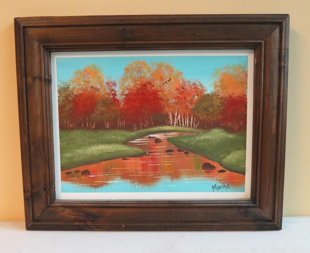 Landscape painting of fall foliage reflecting in a stream, framed in dark wood.