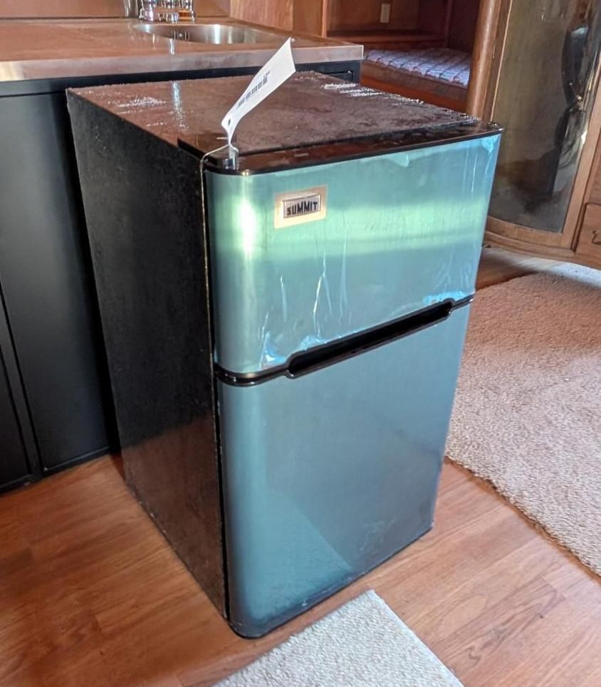 Small black mini fridge with granite top in a kitchen beside a wooden floor and counter