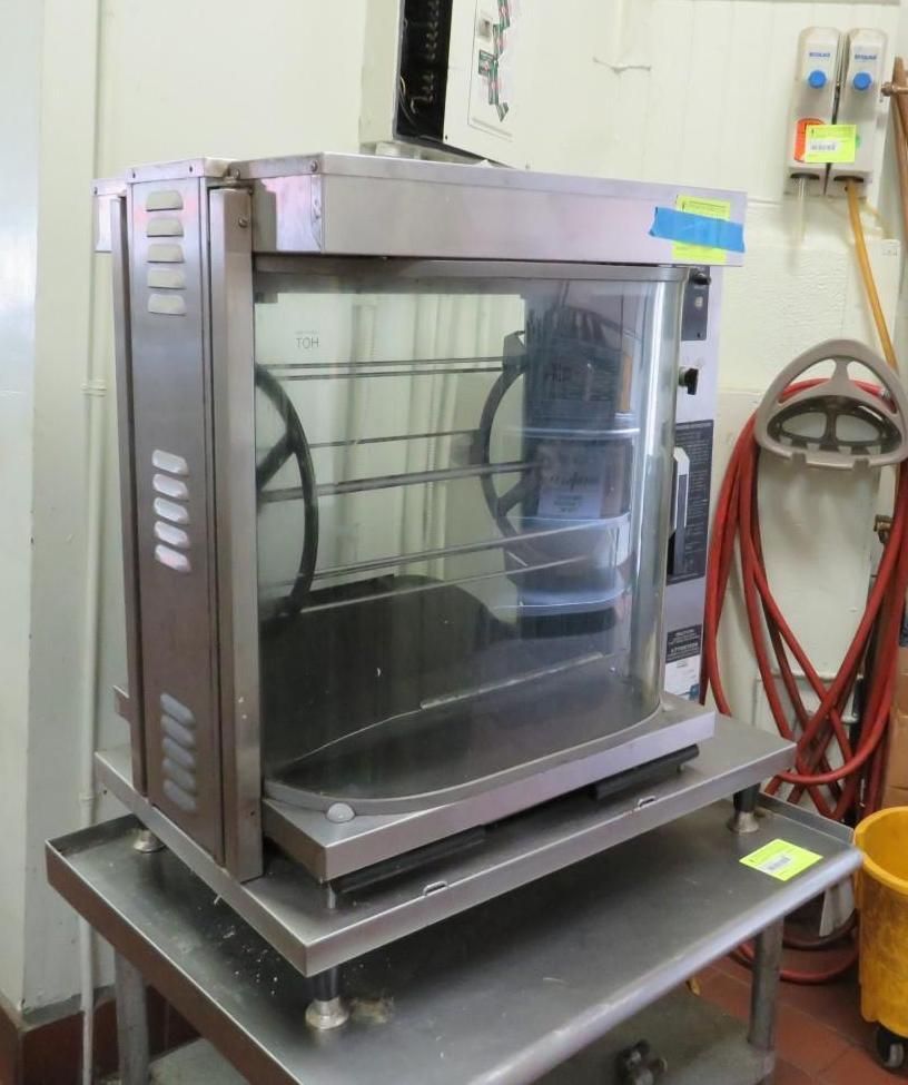 Commercial rotisserie oven on a stainless steel cart, clear glass door.