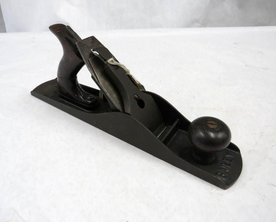 Black and brown hand plane on a white surface, with a wooden handle and knob.
