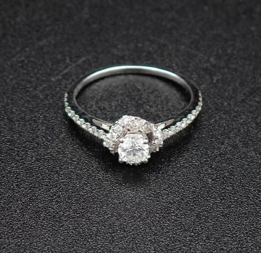 Diamond engagement ring, white gold band with a halo setting, on a dark surface.