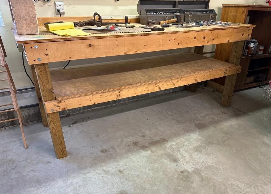 Wooden workbench in a garage with tools on top and a lower shelf.