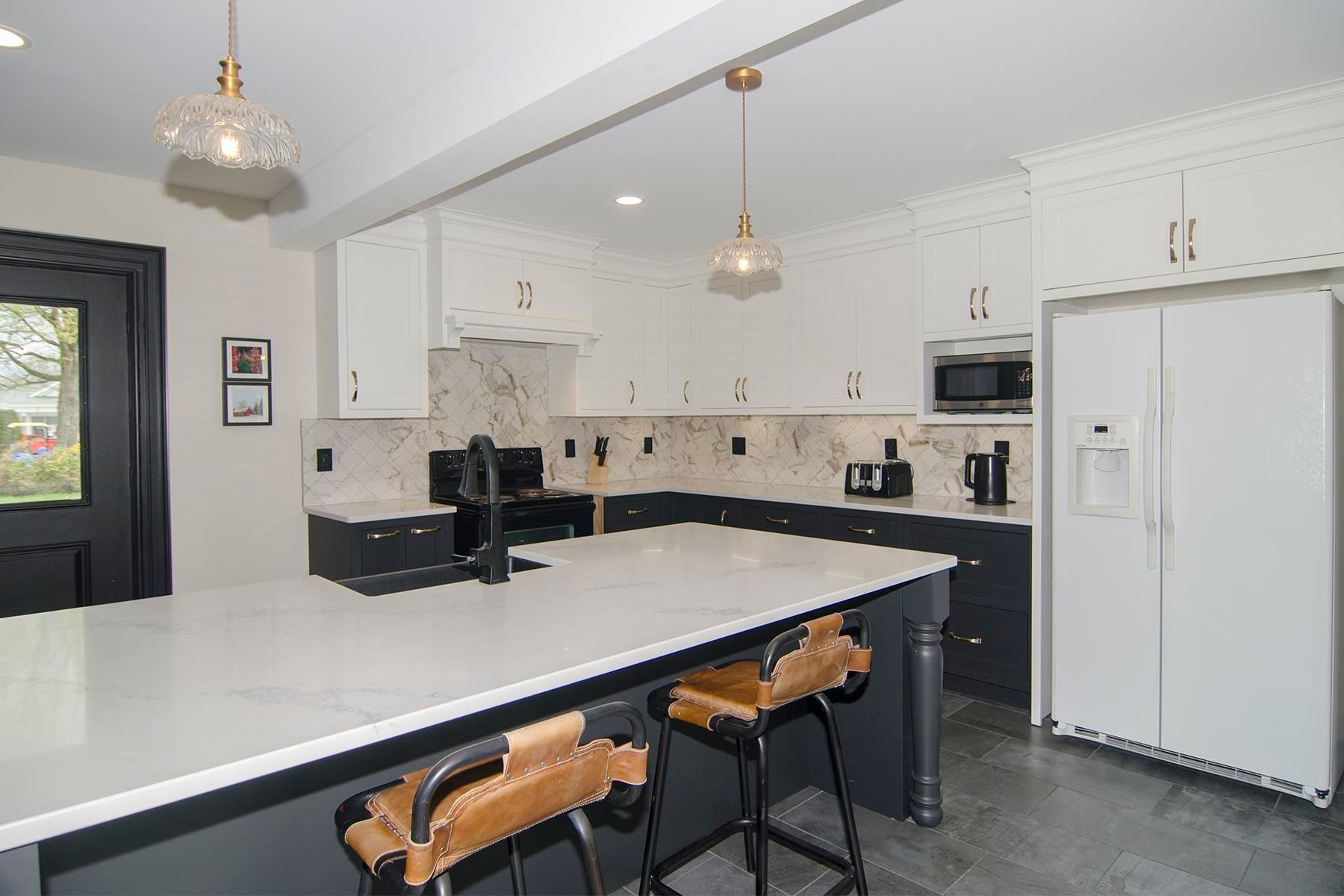 Modern kitchen with white and dark gray cabinets, island with stools, and white countertops.