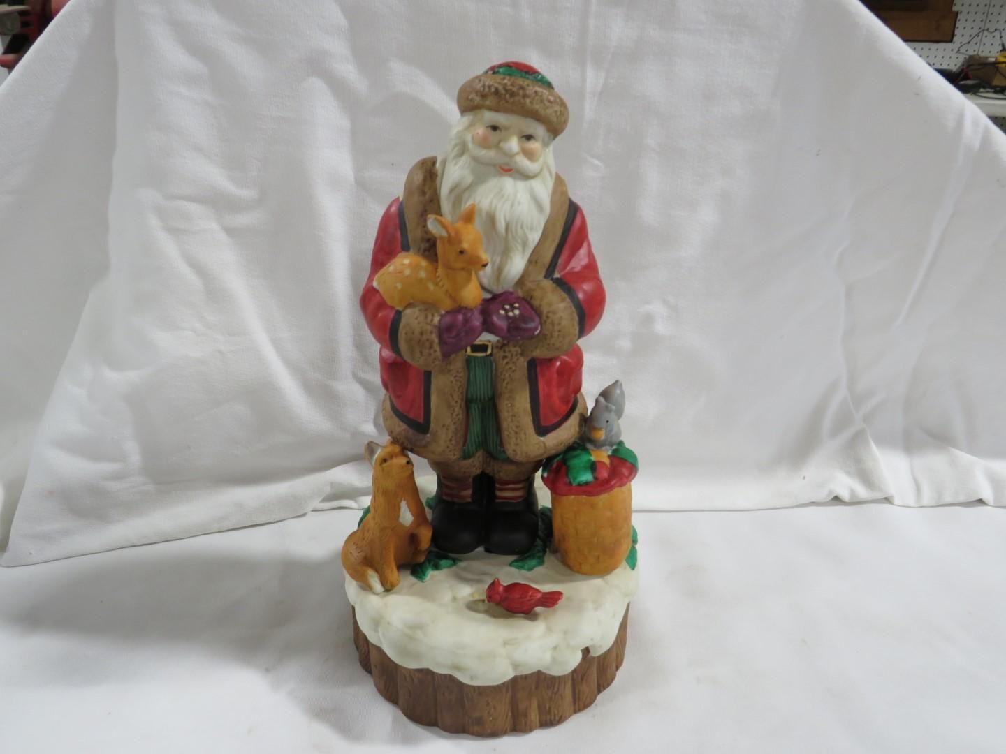 Santa figurine holding a deer and surrounded by forest animals on a snowy base.